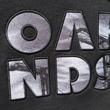 Close up of OAK capital letters with a photo of Oakland cranes in each letter on a black hooded sweatshirt.