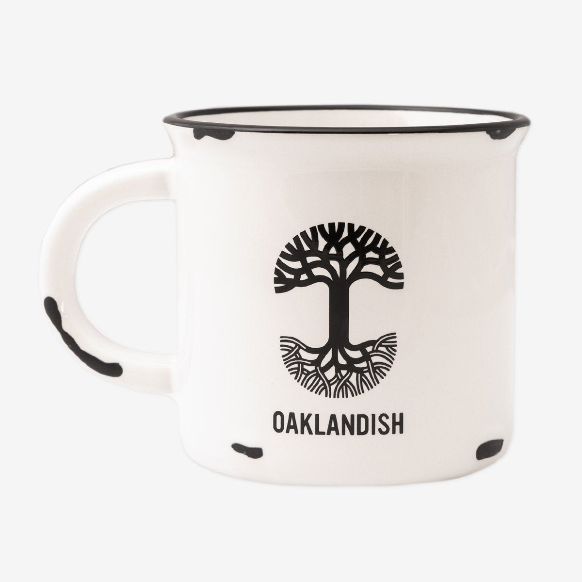 The 15 oz Ventura Mug by Oaklandish features a white ceramic body accented with a black rim and black speckles. The standout design includes a black tree logo with roots extending below it, accompanied by the "OAKLANDISH" text beneath, celebrating Oakland city pride. The handle is thoughtfully designed with matching speckles to complete the cohesive look.