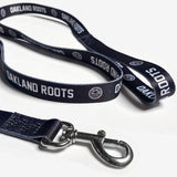 Close-up of black dog leash with white OAKLAND ROOTS wordmark and round full-color logo on repeat.
