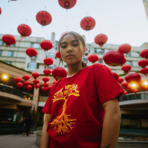 Female model wearing red t-shirt with gold dragon power graphic design in the shape of an Oaklandish tree logo.