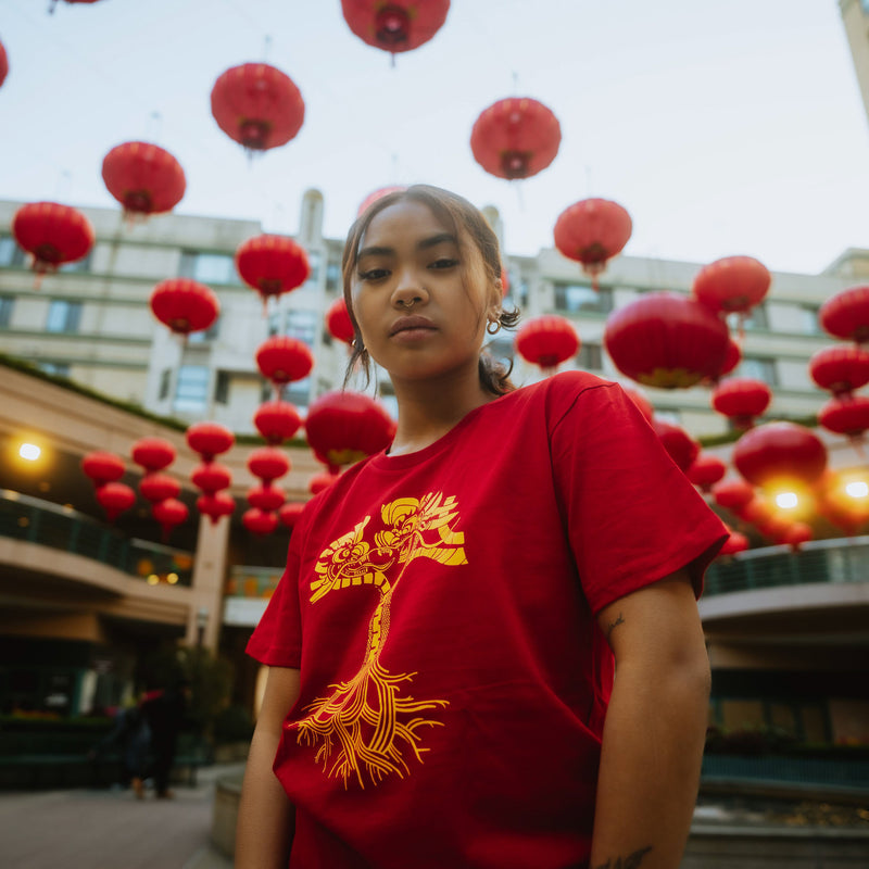 Female model wearing red t-shirt with gold dragon power graphic design in the shape of an Oaklandish tree logo.