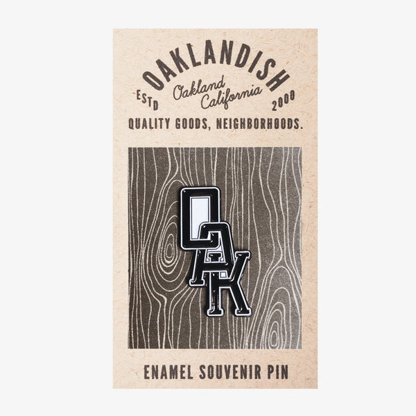  Enamel lapel pin with black OAK wordmark with white trim on brown paper Oaklandish retail packaging. 