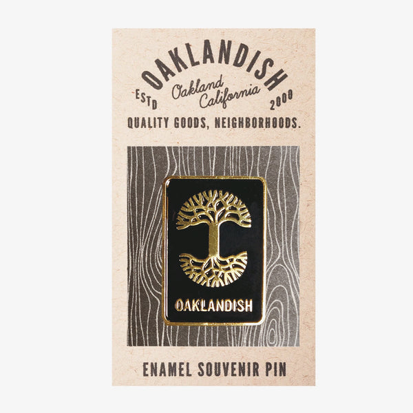 Enamel pin with gold Oaklandish tree logo and wordmark on black background on brown paper retail packaging. 