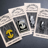 Four Oaklandish enamel lapel pins, two with tree logos, and two with OAK wordmarks, on brown paper Oaklandish retail packaging.