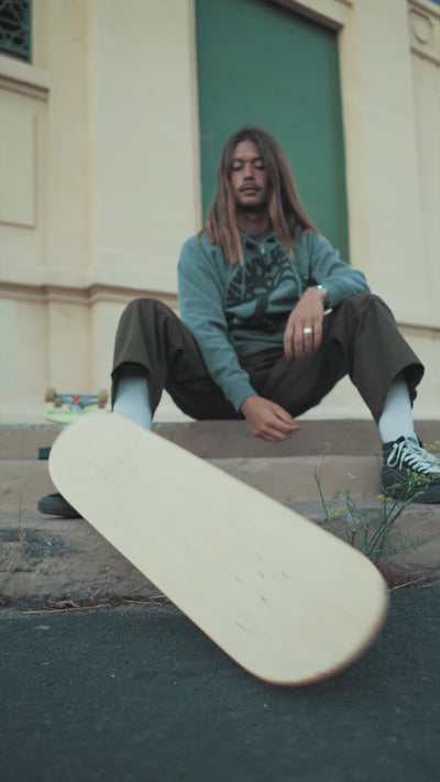 Male model with long hair, seated on a curb setting up  Hiero skate deck, then skating it in the almost dark in Jack London.