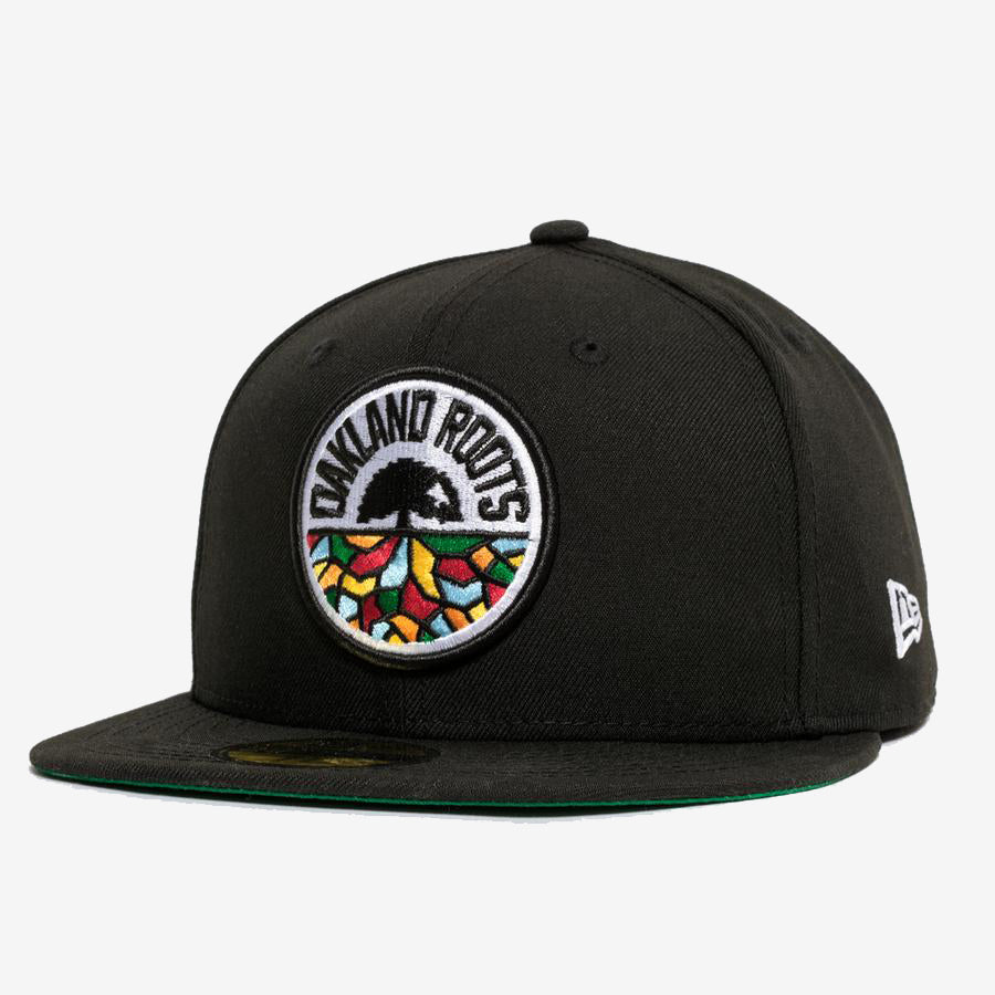 Introducing the New Era Oakland Roots SC 59FIFTY Fitted Cap: a stylish black cap featuring a colorful, circular embroidered logo on the front. This vibrant logo depicts a tree with an intricate root system and "Oakland Roots" text, symbolizing the Oakland Roots SC sports club. The cap includes a flat brim lined with green on the underside and is adorned with a small "New Era" logo on the side.
