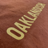 Detailed close up of Oaklandish wordmark in creme ink on a ginger brown shopping tote bag.
