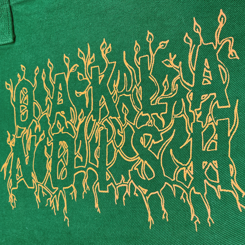 Close-up of creme ink and Oaklandish wordmark surrounded by stems and vines on vintage green tote bag.