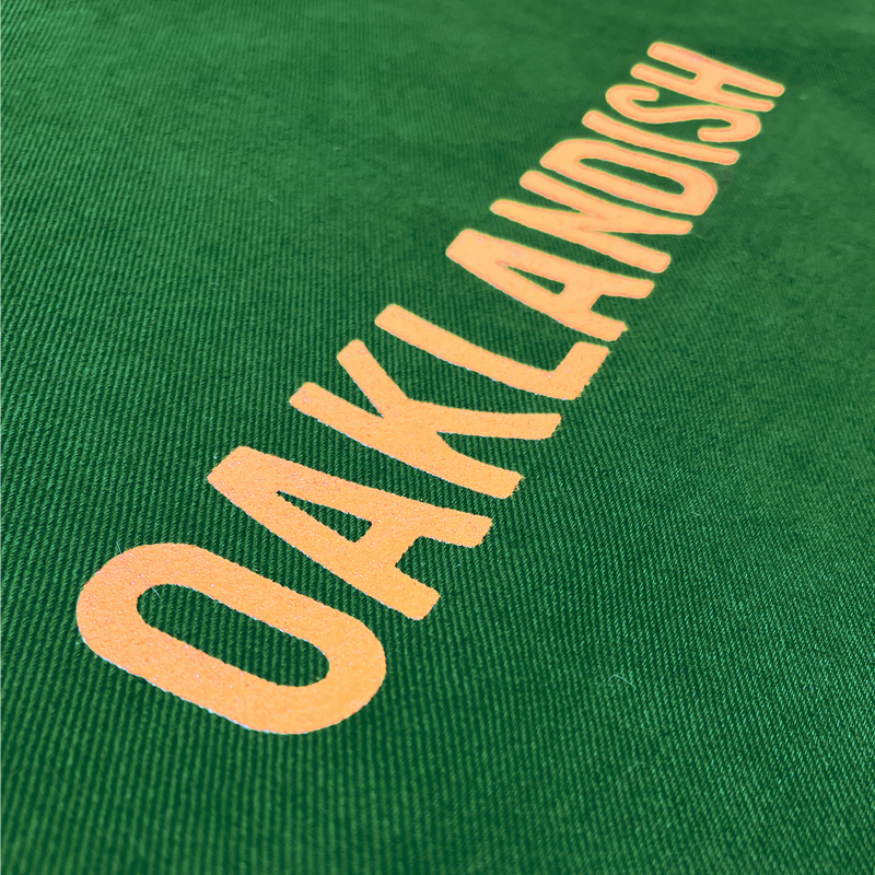 Detailed close up of Oaklandish wordmark in creme ink on a vintage green shopping tote bag.