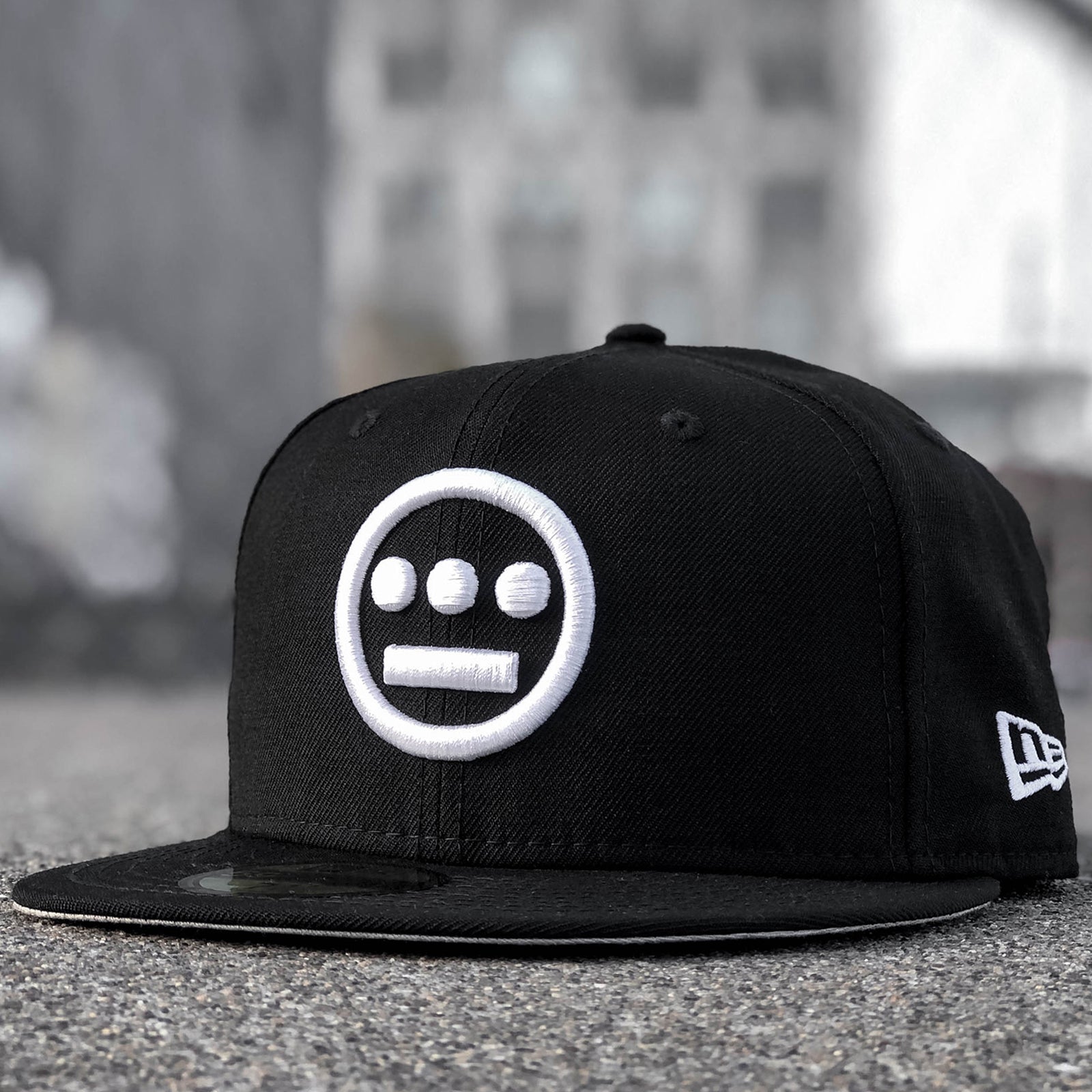 Black cap with white embroidered Hieroglyphics hip-hop logo on the crown and New Era logo on the side on an outdoor sidewalk.