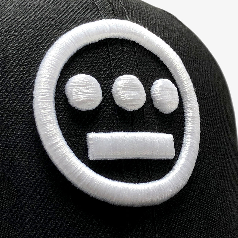 Close-up white embroidered Hieroglyphics hip-hop logo on the crown of a New Era cap.