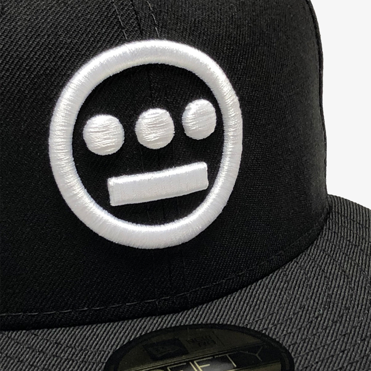 Close-up white embroidered Hieroglyphics hip-hop logo on the crown of a New Era cap.