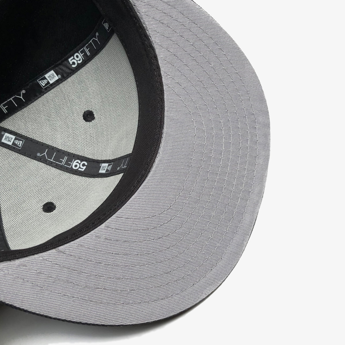 The grey underside of the bill on a New Era black cap.