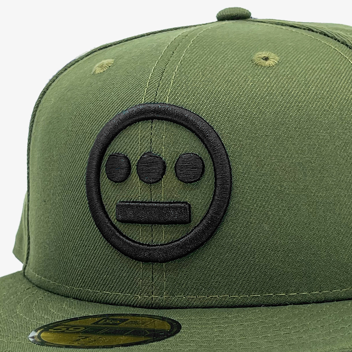 Close-up of black embroidered Hieroglyphics hip-hop logo on the crown of a green New Era cap.