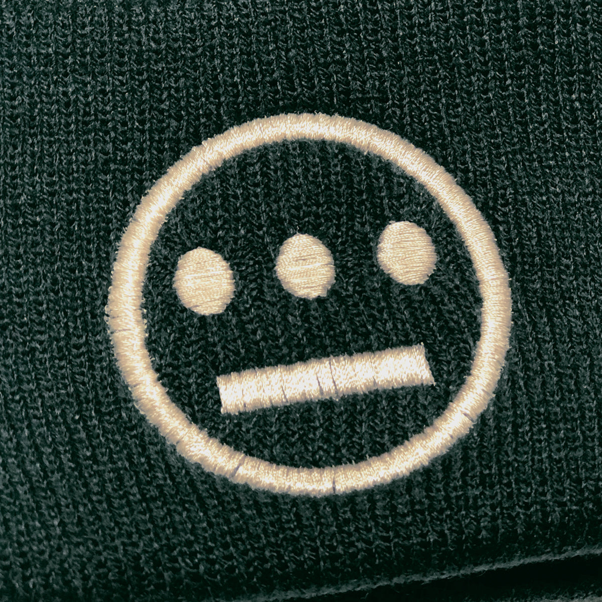 Close up of yellow embroidered Hiero hip-hop crew logo on the cuff of forest green beanie.