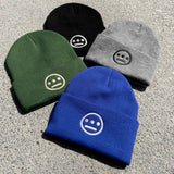 Close-up of 4 cuffed acrylic beanies in green, blue, black & grey, with white embroidered Hiero logos on on asphalt.