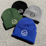 Close-up of 4 cuffed acrylic beanies in green, blue, black & grey, with white embroidered Hiero logos on on ashpalt.