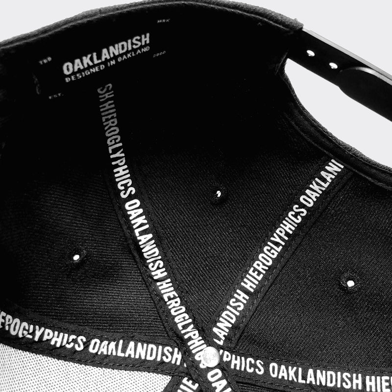 Underside of black dad cap with OAKLANDISH wordmark on inside striping on in crown and Oaklandish logo patch on rim.