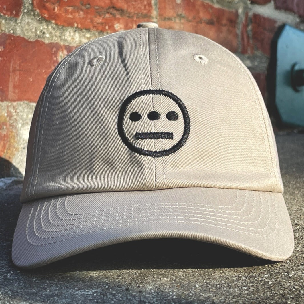 Khaki dad cap with black embroidered Hiero hip-hop crew logo on crown outside with brick wall background. 