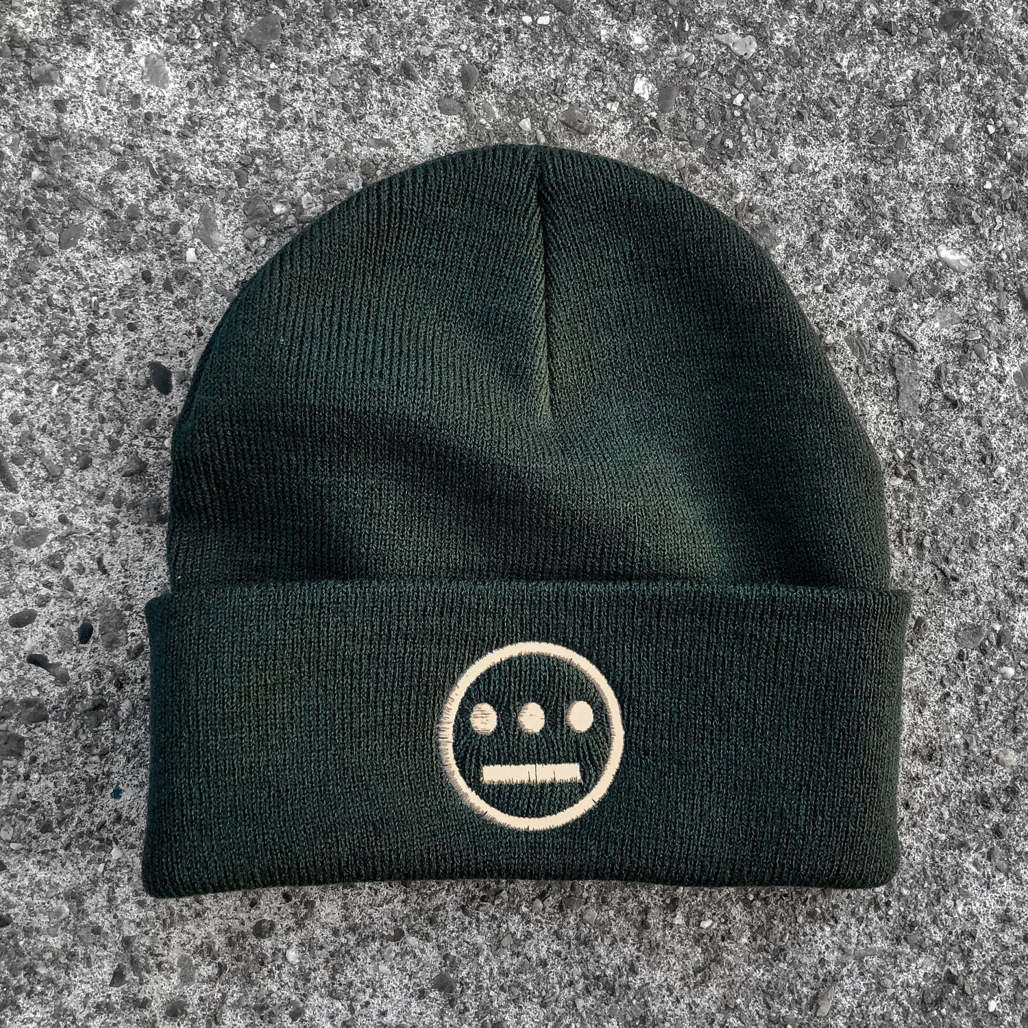 Forest green cuffed beanie with cream Hiero hip-hop crew logo on cuff on asphalt. 