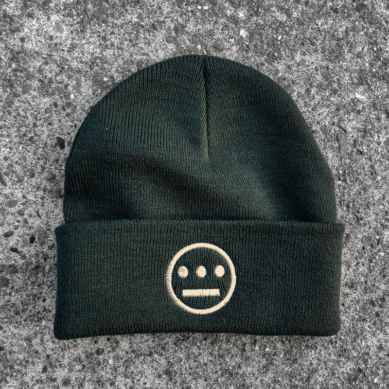 Forest green cuffed beanie with cream Hiero hip-hop crew logo on cuff on asphalt. 