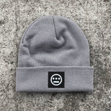 Grey cuffed beanie with black and white hiero hip-hop logo patch on the cuff on asphalt.