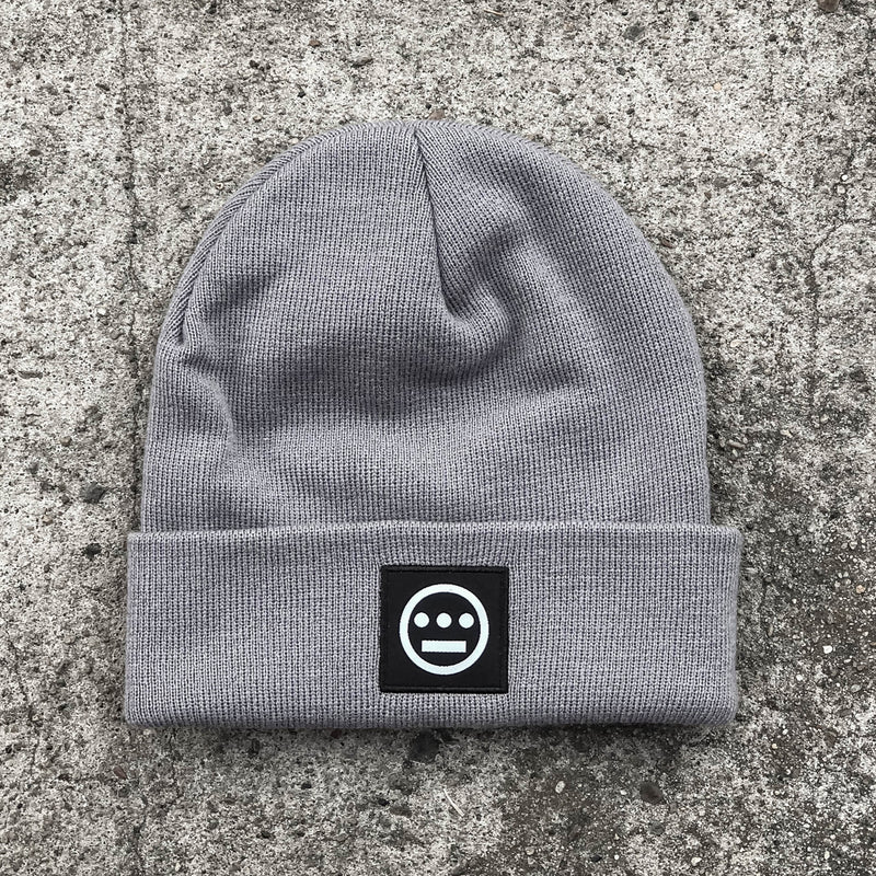 Grey cuffed beanie with black and white hiero hip-hop logo patch on the cuff on asphalt.