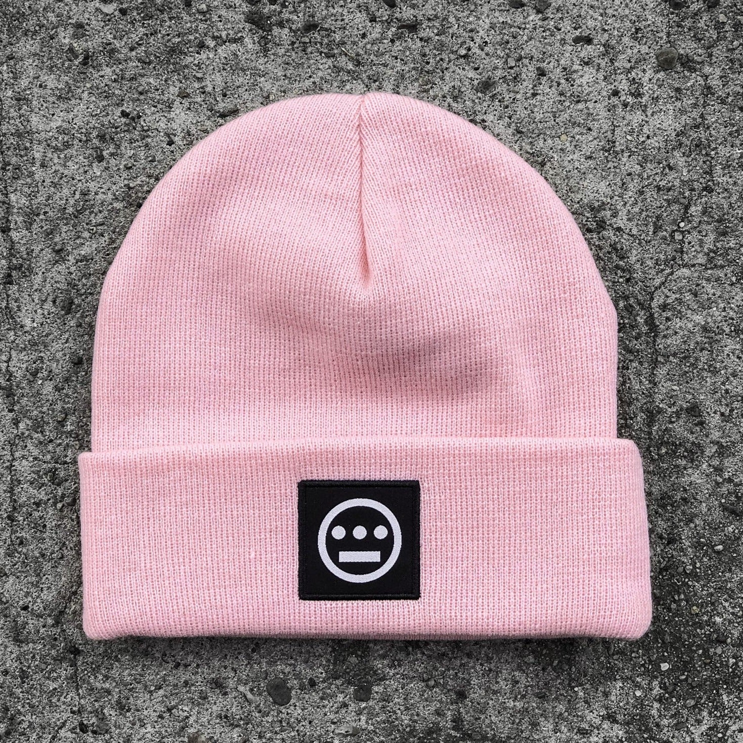 Pink cuffed beanie with black and white hiero hip-hop logo patch on the cuff on asphalt.