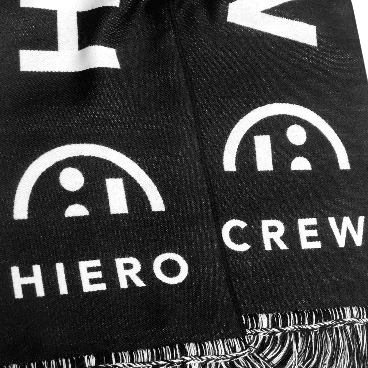 Detailed close-up of HIERO and CREW wordmarks on the two ends of a black woven scarf.