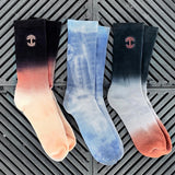 The three color choices of Oaklandish dip-dyed men’s crew socks (dusk haze, dawn fog, and blue and white) on a wood deck. 