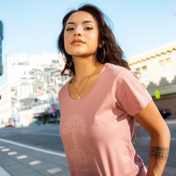 Women on Oakland street wearing pink scoop neck t-shirt with Oaklandish tree logo and wordmark on the chest.