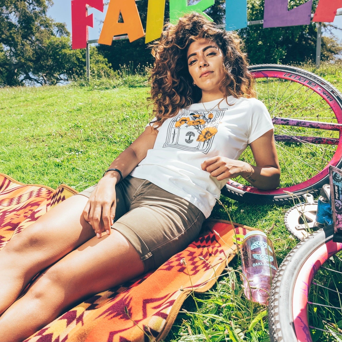 A woman lying on a picnic blanket in Oakland Fairyland with a bike wearing an Oaklandish Blossom t-shirt.