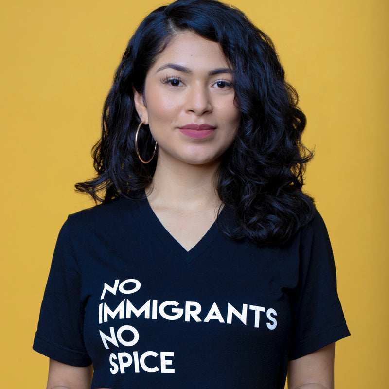  Women wearing a black V-Neck t-shirt with white No Immigrants, No Spice wordmark. Image has a yellow background.