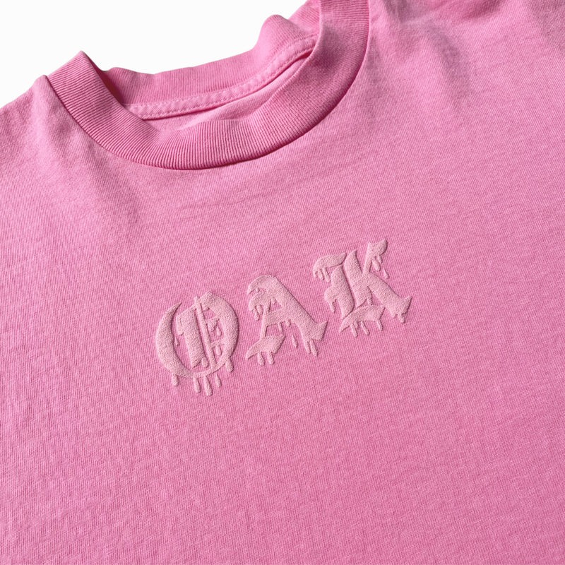 Close-up of OAK wordmark in old style font with a bleed on a pink t-shirt.  