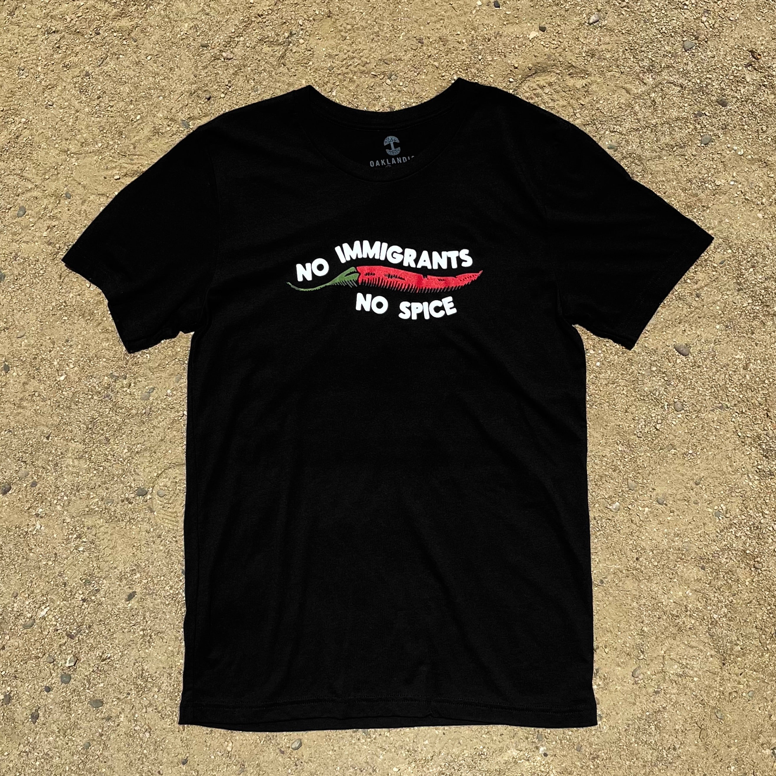 Black t-shirt with No Immigrants, No Spice wordmark, and red chili pepper laying on sand.