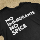 Close-up of a black t-shirt with white No Immigrants, No Spice wordmark laying on the sand.