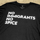 Close-up of black V-neck t-shirt with white No Immigrants, No Spice wordmark laying on sand.