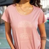 Women on Oakland street, view of her waist to the chin, wearing pink scoop neck t-shirt with Oaklandish tree logo and wordmark on chest.