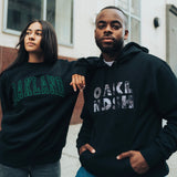 A woman and a man standing outdoors in Oakland wearing black Oaklandish sweatshirts.
