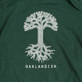 Close-up of the white Oaklandish tree logo and wordmark on the chest of a forest green infant one-piece.