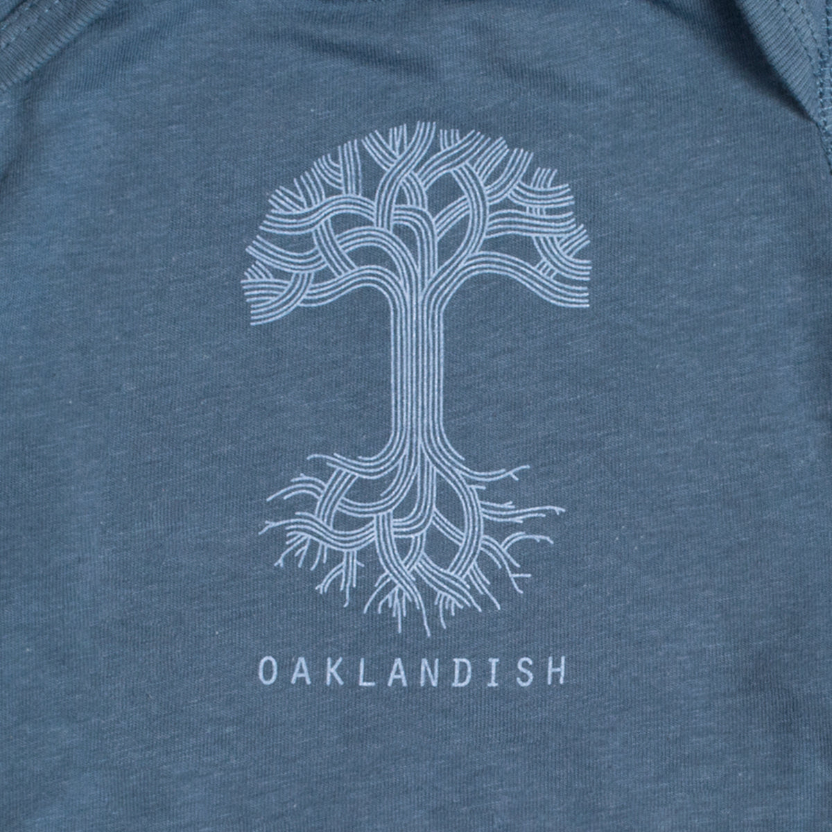 Close-up of light blue Oaklandish tree logo and wordmark on the chest of an indigo infant one-piece.