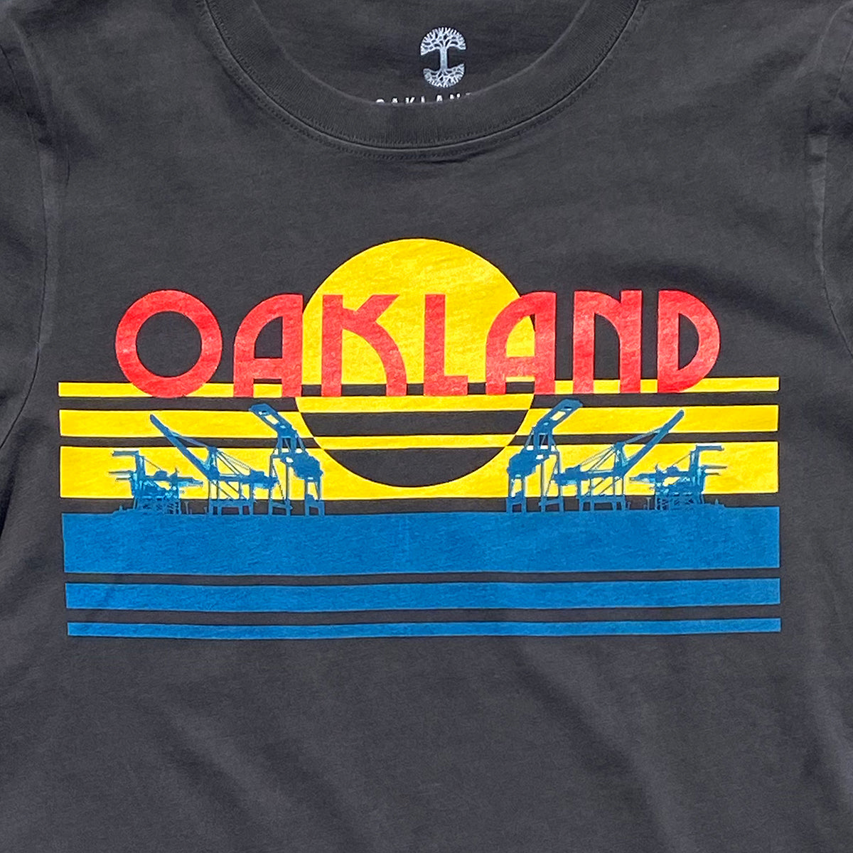 Close-up of multi-color license plate design with capital letters spelling out OAKLAND on faded black women’s t-shirt.