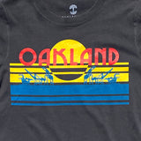 Close-up of multi-color license plate design with capital letters spelling out OAKLAND on faded black women’s t-shirt.