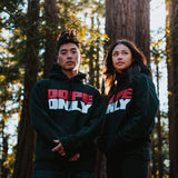 Man and woman standing in a forest wearing black hoodies with large red and white DOPEONLY wordmark logos on the chests.