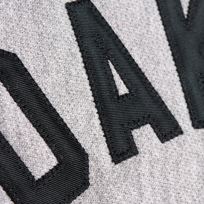 Detailed close-up stitching on black applique OAKLAND ROOTS wordmark on the chest of a grey crew sweatshirt.