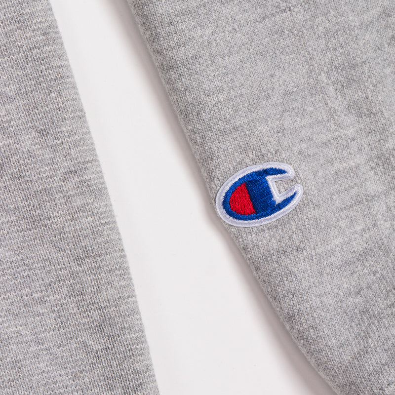Red and blue embroidered Champion logo on the sleeve of grey OAKLAND ROOTS crew sweatshirt.