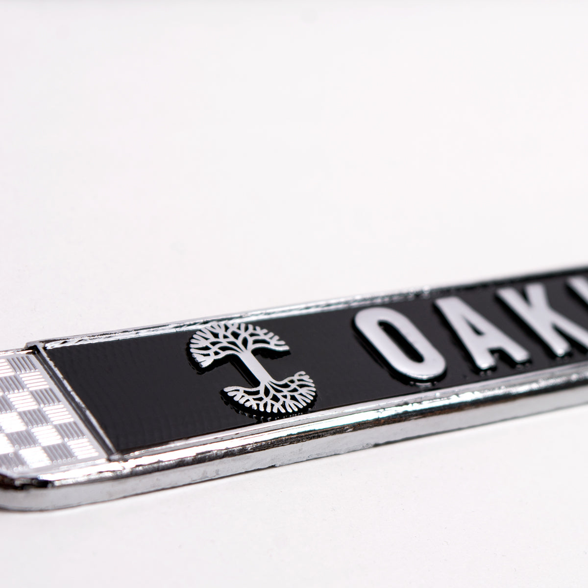 Detailed close-up of silver Oaklandish tree logo on the bottom black rim of a license plate holder.
