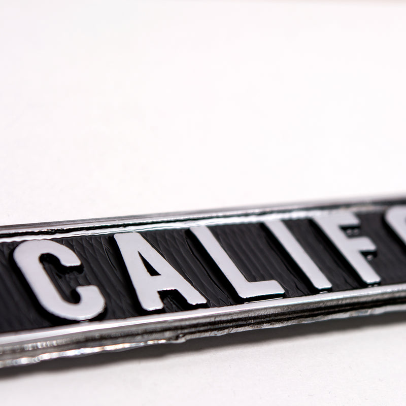 Detailed close-up of silver California wordmark on the bottom black rim of a license plate holder.