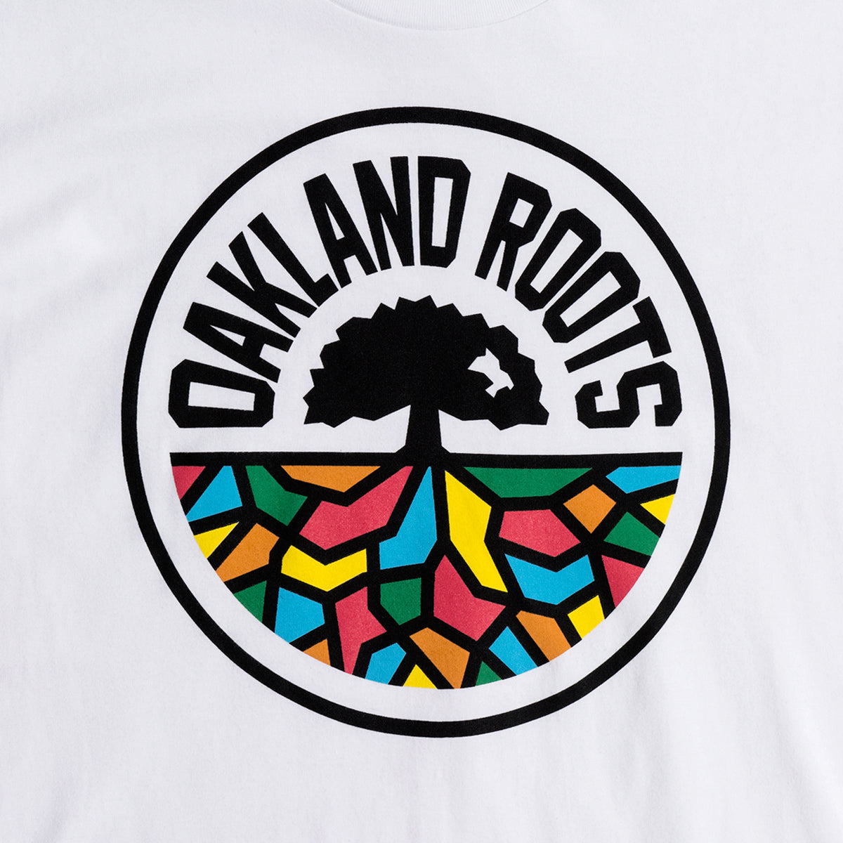 Close up of full-color, round Oakland Roots logo on the chest of a white t-shirt. 
