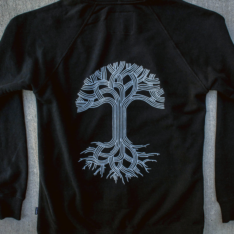 The back side of a black hooded sweatshirt with a white Oaklandish tree logo on the back.
